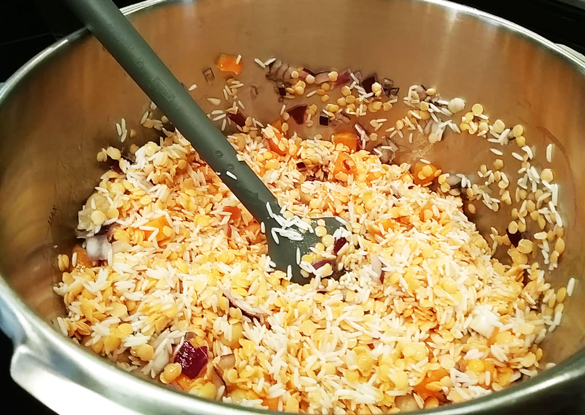 She heated oil in the second pressure cooker and added the rice and lentil mix as well as the onions and garlic.